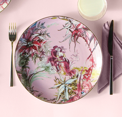 Decorative plate with floral and fairy design on a pink table setting with cutlery and a glass.