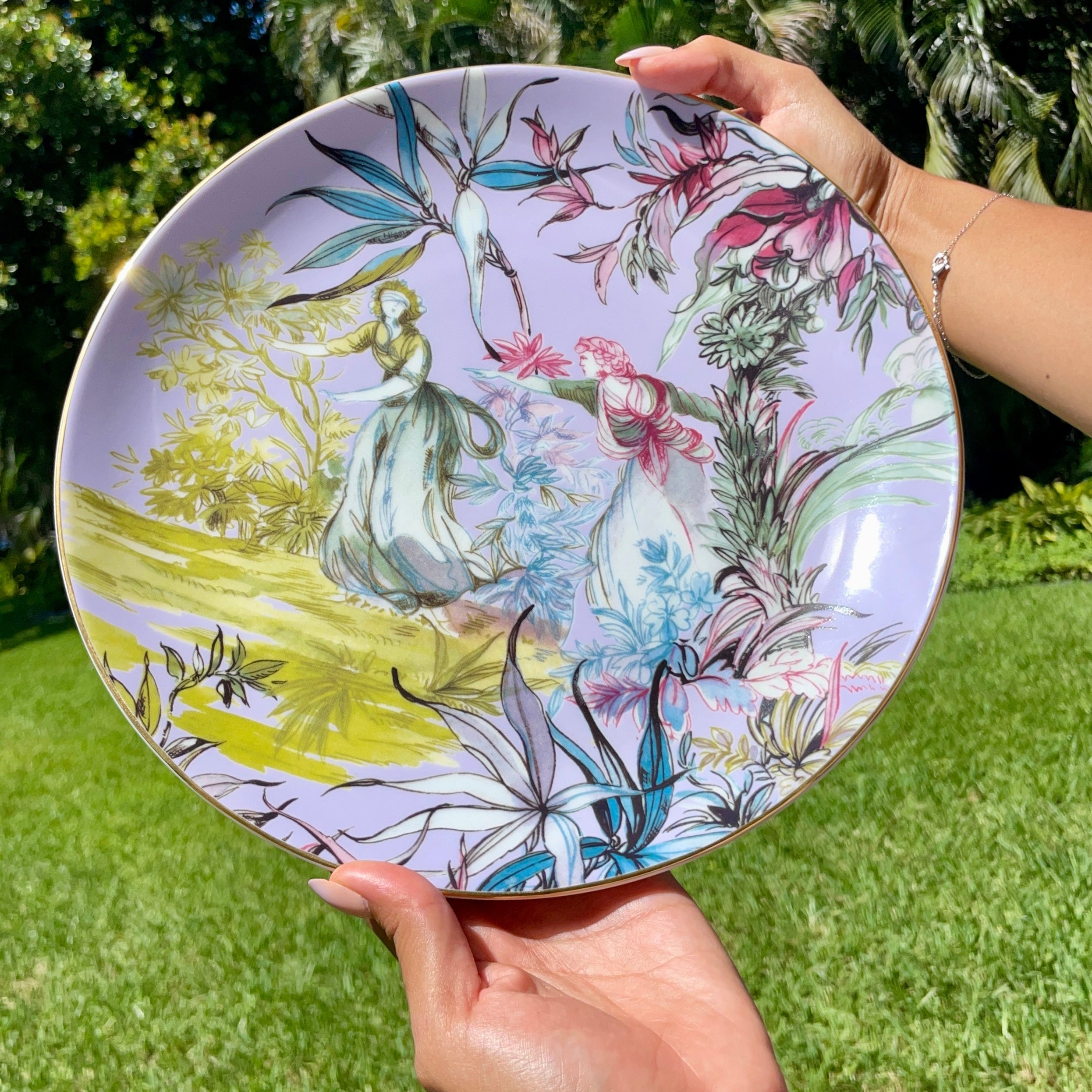 Person holding a decorative plate with floral and fairy design outdoors