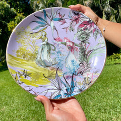 Person holding a decorative plate with floral and fairy design outdoors