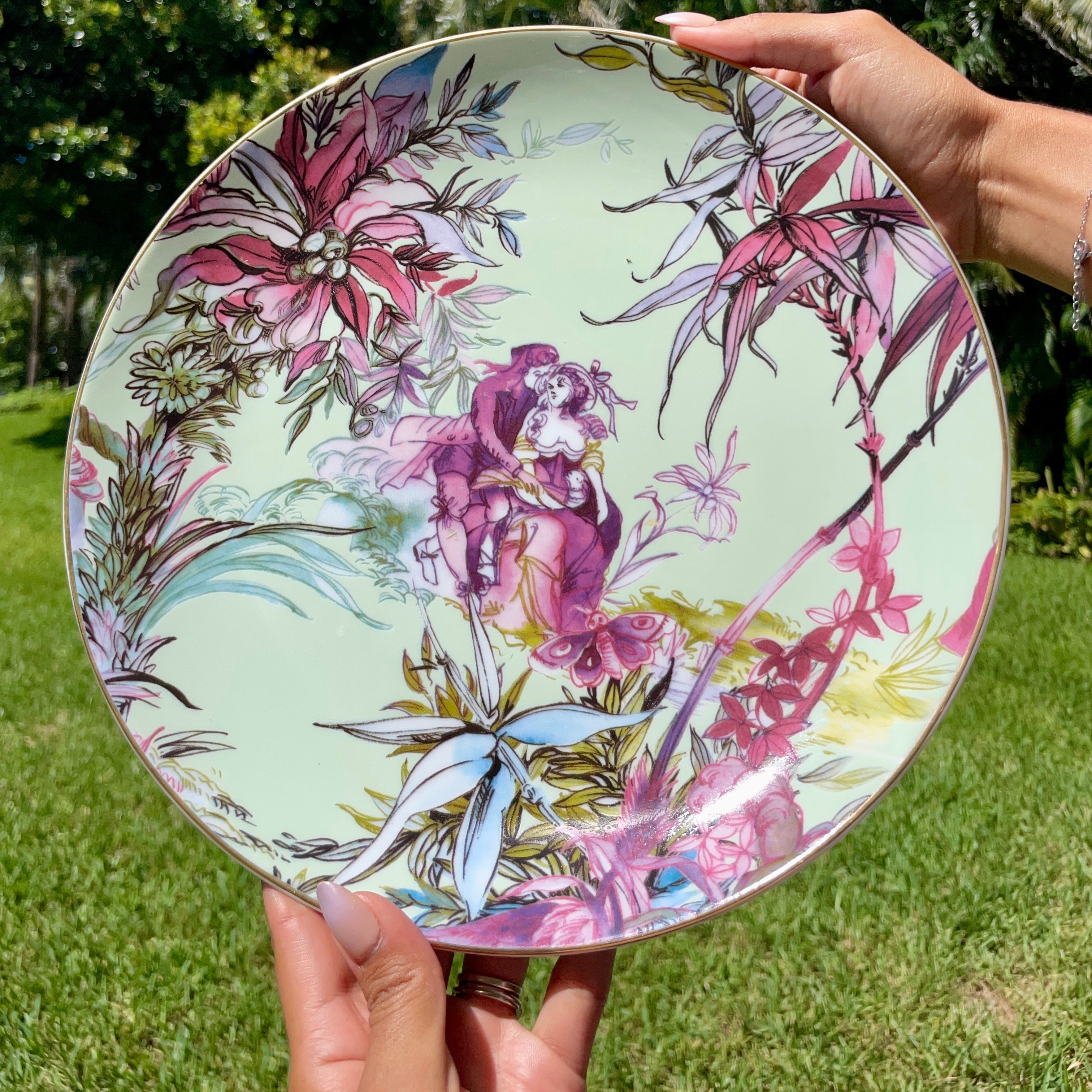 Person holding a decorative plate with floral and fairy design outdoors.