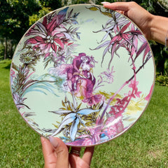 Person holding a decorative plate with floral and fairy design outdoors.