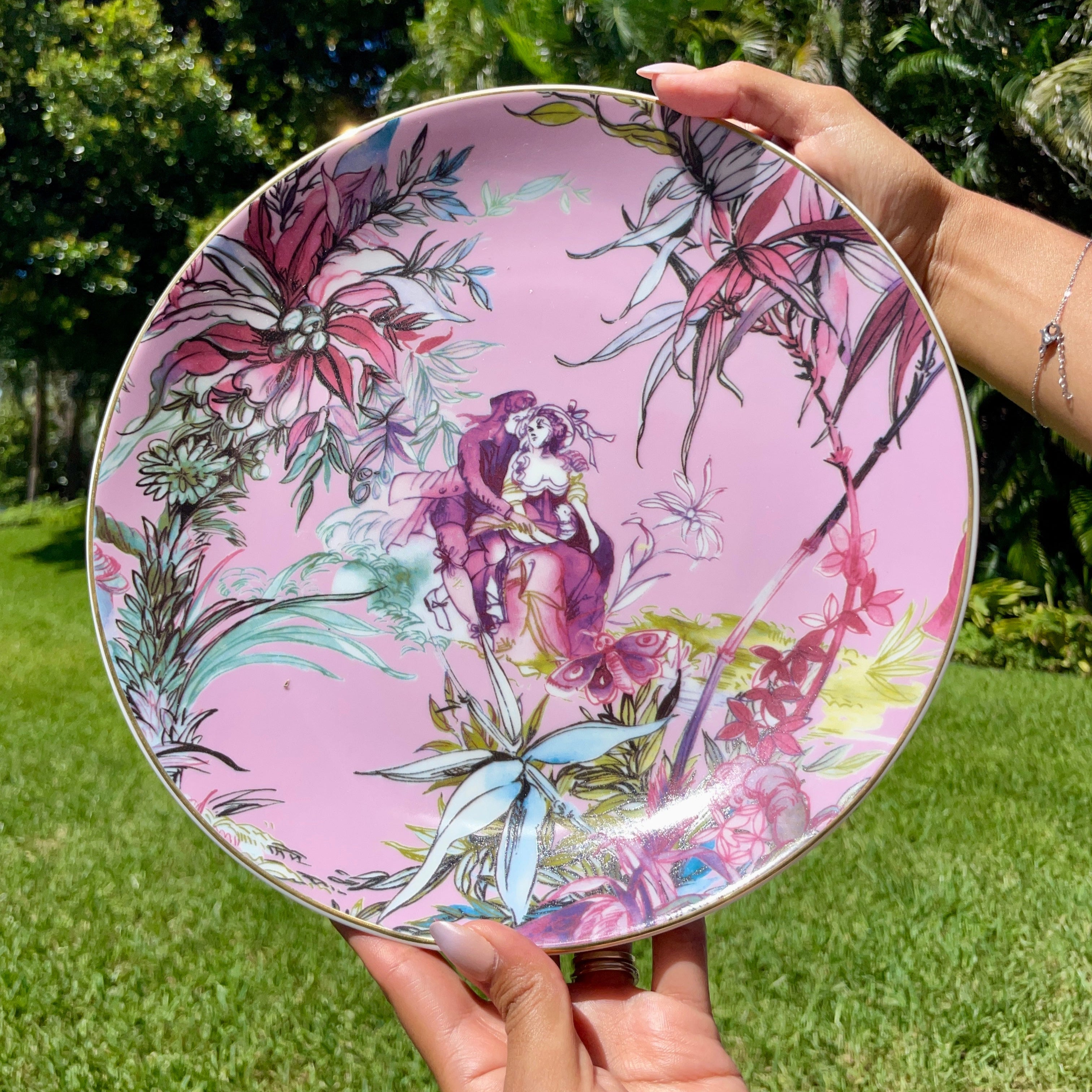 Person holding a decorative plate with floral and butterfly design outdoors.